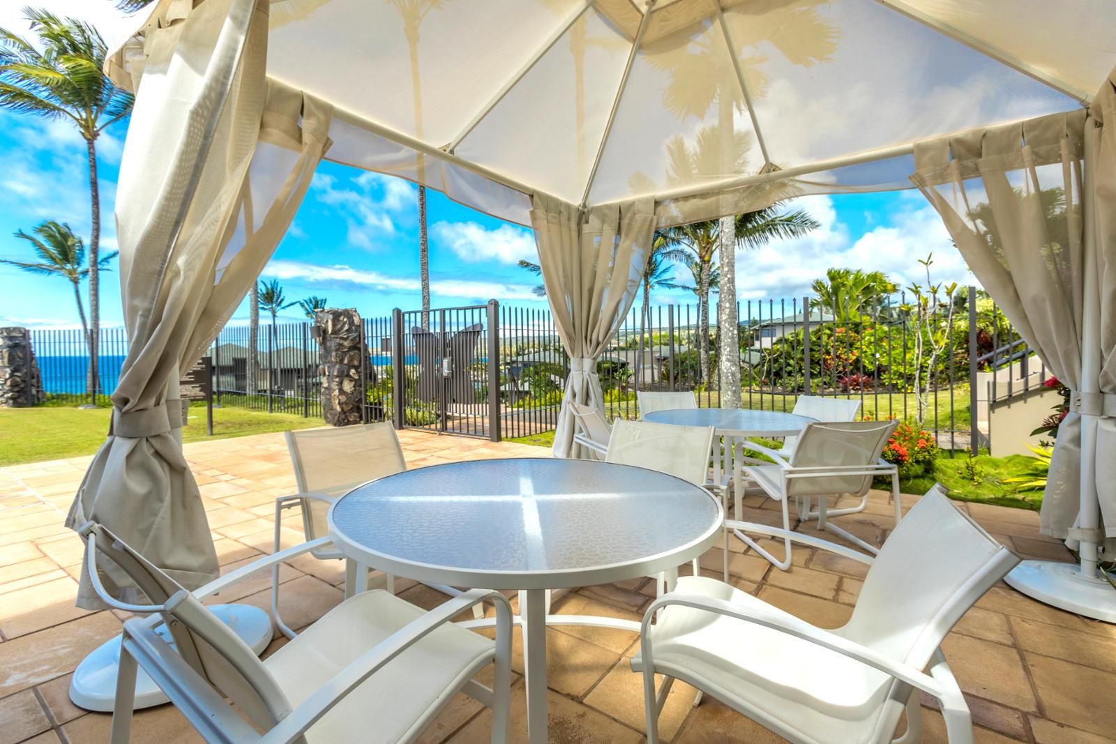 An outdoor patio with a covered seating area, white chairs, and a round table.