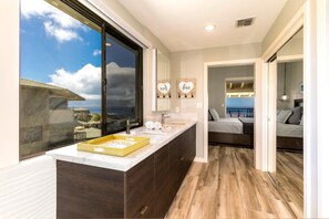 Ein modernes Badezimmer mit einem großen Fenster, einem Waschtisch mit einer gelben Seifenschale und Blick aufs Meer.