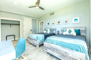 A bedroom with two beds, a ceiling fan, a desk, and a chair.