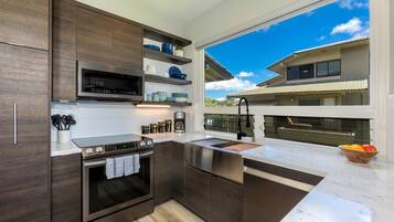 A modern kitchen with dark wood cabinets, stainless steel appliances, and a large window offering a view of a house.