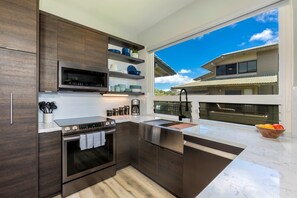Eine moderne Küche mit dunklen Holzschränken, Edelstahlgeräten und einem großen Fenster mit Blick auf ein Haus.