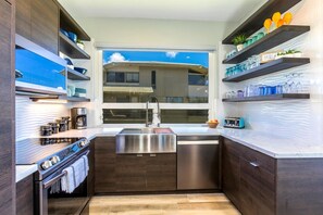 A modern kitchen with dark wood cabinets, stainless steel appliances, and a window with a view of a building. - Kapalua Bay Villas | Ocean View 2 BR | Car Incl. w/ 6+ Nights | KBV-32B2 by KBM (Lahaina)