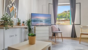 A modern living room with a flat-screen TV, a dining area with a table and chairs, a view of a mountainous landscape through a window, and a decorative wall piece. - SPACIOUS HOUSE IN HISTORIC CENTER WITH MAGNIFICENT VIEWS (Sagunt)