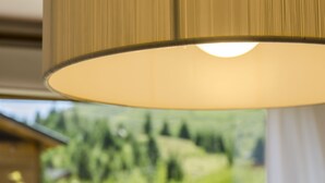 Ein Nahblick auf eine Lampe mit geripptem Schirm, ein Fenster mit Blick auf eine grüne Landschaft und ein teilweise sichtbarer weißer Vorhang.