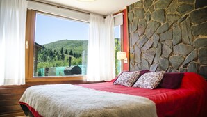 Ein Schlafzimmer mit großem Fenster, einer Steinsäule und einer roten Bettdecke.
