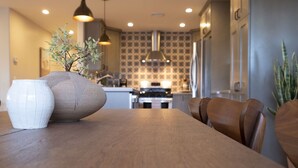 A dining area with a wooden table and chairs, a vase with a plant, and a kitchen in the background. - Sunrise to moonrise views. Hike/bike out the door. (Sedona)