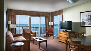A hotel room with a sofa, armchairs, a dining table, a TV, and a view of the ocean through large windows. - Luxury Ocean Front 3 Bedroom, 18th Floor at Bayview Resort, Myrtle Beach (Myrtle Beach)