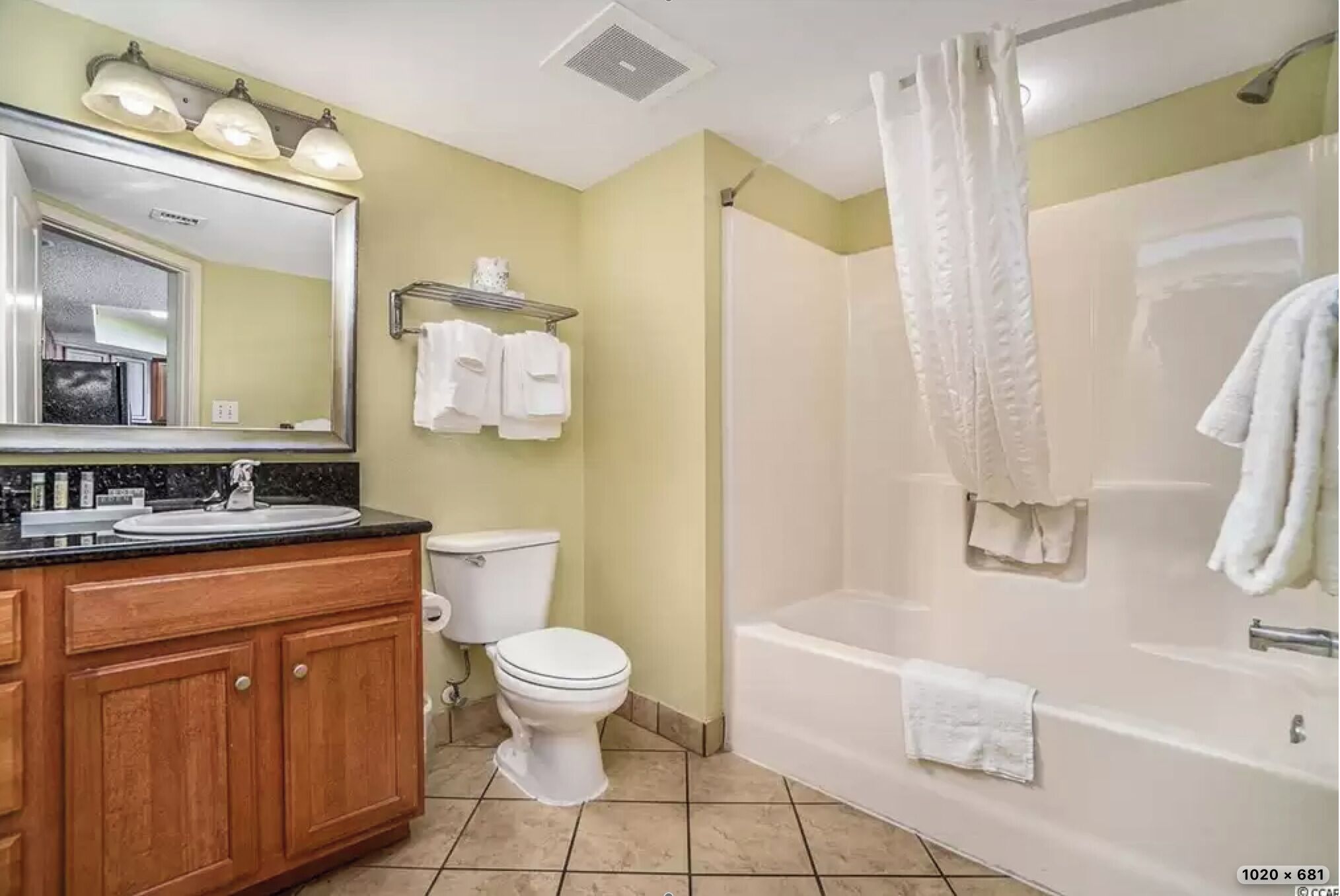 A bathroom with a wooden vanity, a toilet, a bathtub, and a shower curtain.