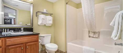 A bathroom with a wooden vanity, a toilet, a bathtub, and a shower curtain.
