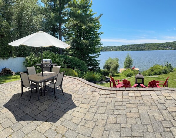 Une terrasse extérieure avec une table et des chaises, un barbecue et des fauteuils Adirondack rouges.