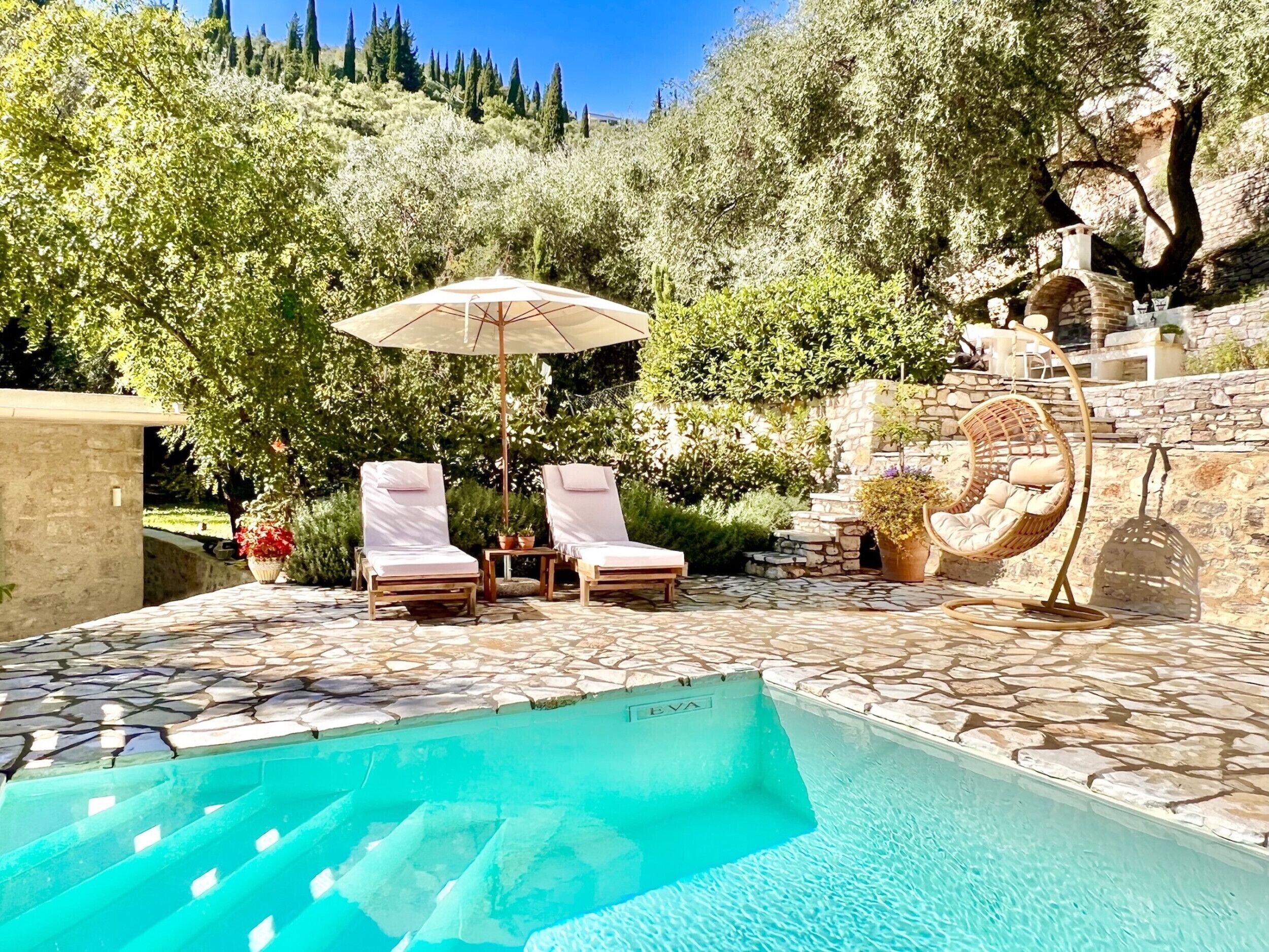 A pool area with lounge chairs, a hanging chair, and a stone wall.