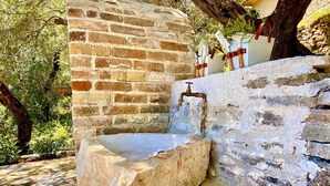 A stone well with a metal spout, surrounded by a stone wall and trees. - Villa Eva Agni with private pool (Agni)