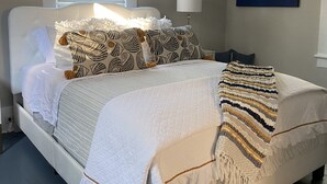 Un lit bien fait, agrémenté d’oreillers à motifs, d’une couverture blanche et d’un plaid rayé.