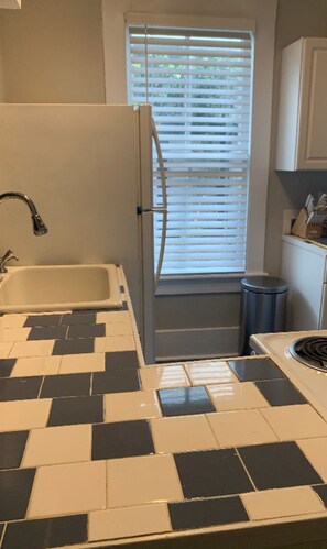 Een keuken met een betegelde spatwand, een koelkast, een spoelbak en een raam met zonwering.