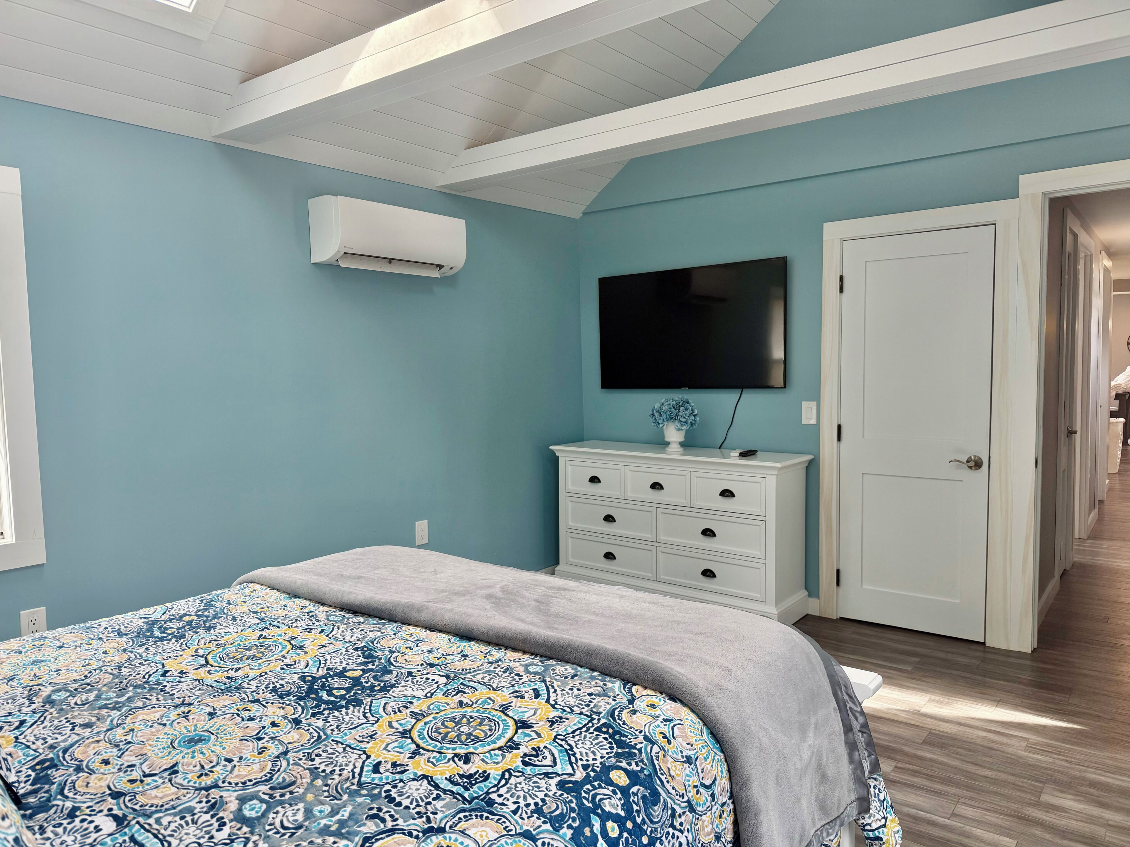 A bedroom with a bed, a dresser, a television, and an air conditioning unit.