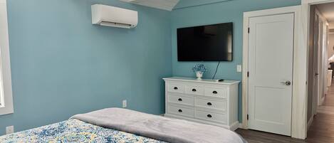 A bedroom with a bed, a dresser, a television, and an air conditioning unit.