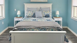 A bedroom with a bed, two bedside tables, a ceiling fan, a window, and a wall-mounted artwork. - Gateway to Acadia Renovated Milbridge Coastal Home (Milbridge)