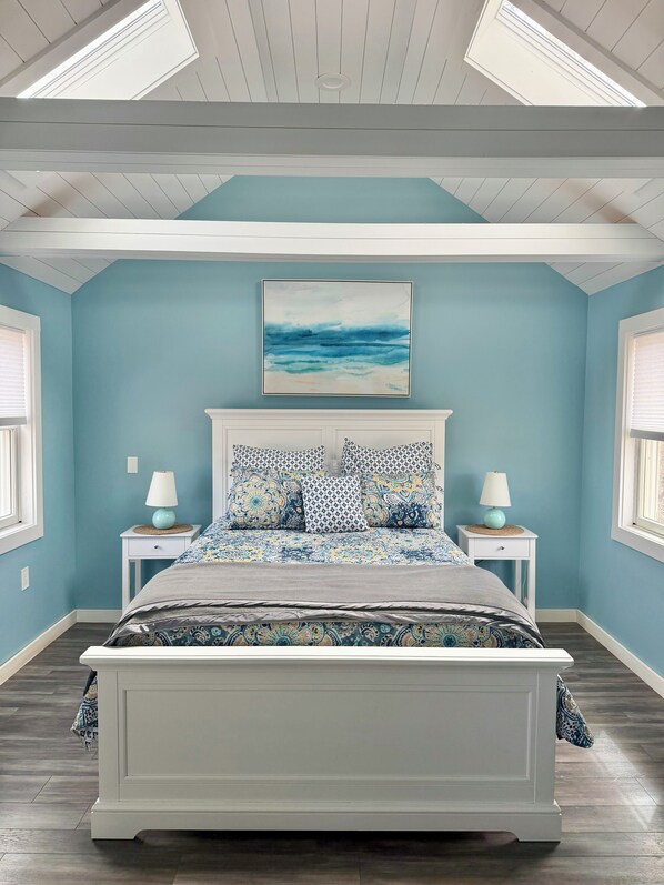 A bedroom with a bed, two bedside tables, a ceiling fan, a window, and a wall-mounted artwork.