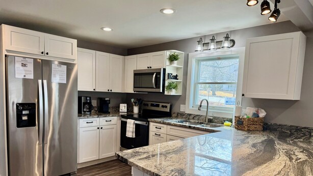 A modern kitchen with white cabinets, stainless steel appliances, a granite countertop, and a window with a view. - Gateway to Acadia Renovated Milbridge Coastal Home (Milbridge)