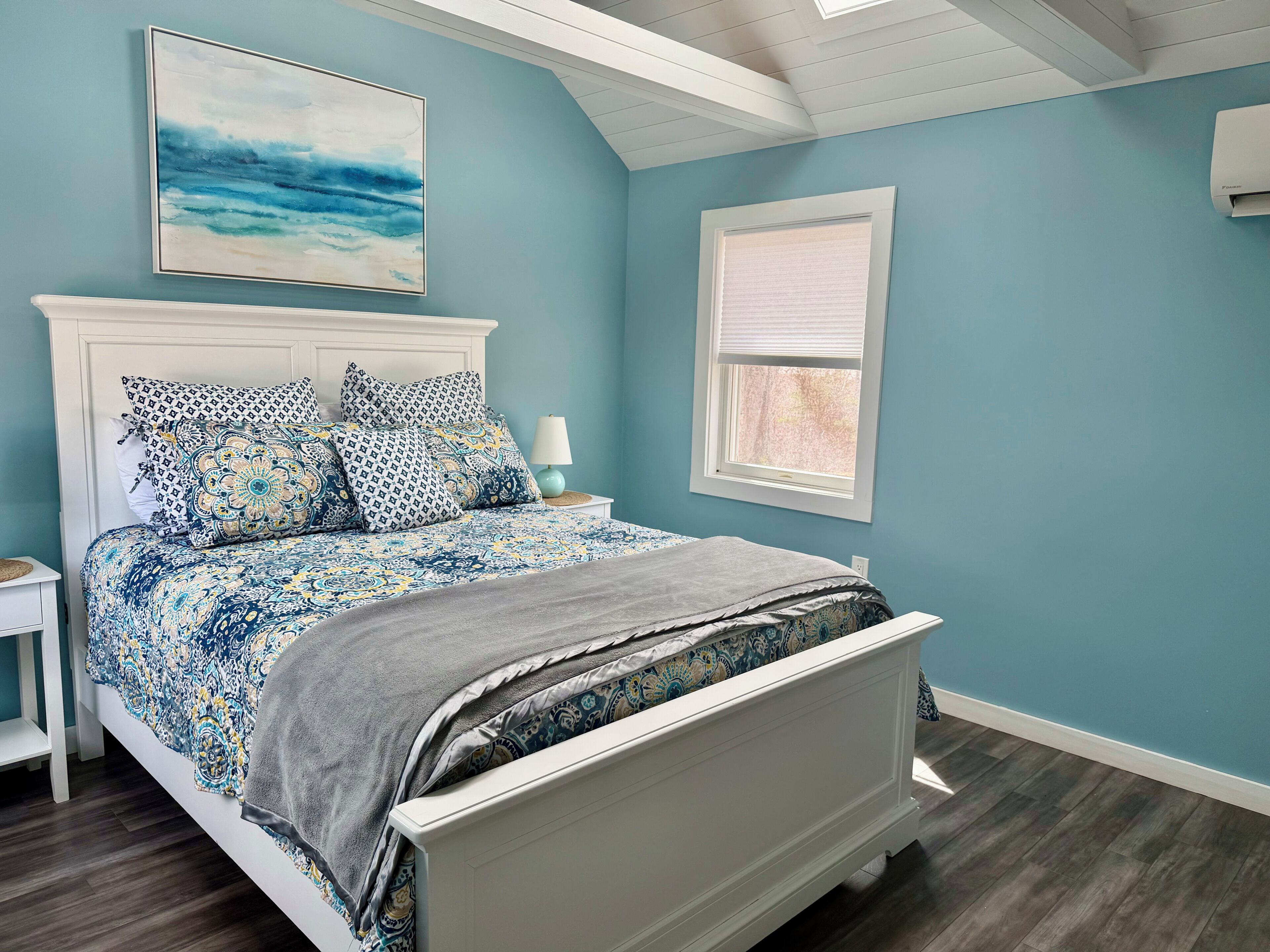 A bedroom with a bed, a nightstand, a lamp, a window, and a ceiling with a skylight.