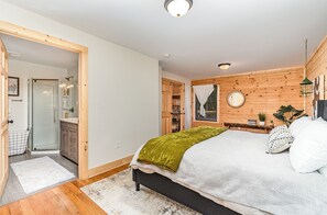 A bedroom with a bed, a wooden headboard, a bedside table with a lamp, and a window with curtains.