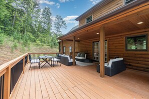 A wooden cabin with a deck, outdoor seating, and a view of the surrounding forest.