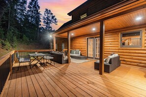 A wooden cabin with a deck, outdoor seating, and a covered porch.