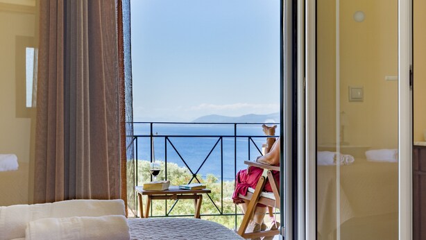 Ein Schlafzimmer mit einem großen Bett, Meerblick und einem Balkon mit Tisch und Stuhl.