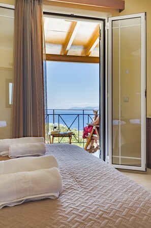 A bedroom with a large bed, a view of the sea, and a balcony with a table and chair.