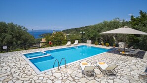 Ein Pool mit Steinboden, Liegestühlen und Blick aufs Meer.