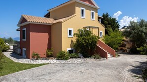 Ein zweistöckiges Haus mit einem Kiesweg, der zum Eingang führt, umgeben von viel Grün und blauem Himmel.