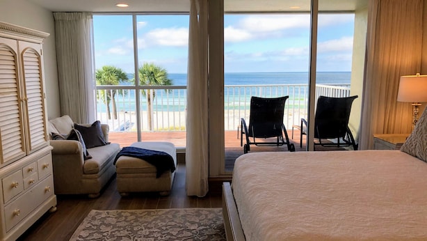 A bedroom with a large bed, a sofa, a chair, and a view of the ocean through large windows. - Luxury 3BD Beachfront Living: La Playa 203D by RVA (Longboat Key)