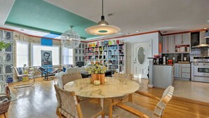 A spacious living room with a large round table, comfortable seating, a bookshelf filled with books, and a kitchen area in the background. - 2 Bedroom/2 Bathroom Stylish Designer Flat (San Francisco)