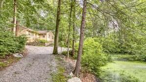Ein Kiesweg führt zu einem Haus, umgeben von Bäumen und einem Teich.