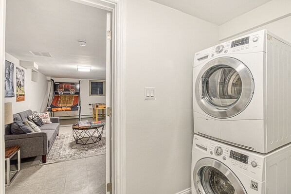 A laundry room with stacked washers and dryers, a gray sofa, and a small table with magazines.