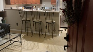 A kitchen with wooden cabinets, a stainless steel refrigerator, and a bar area with three stools. - JC's Place #1 (Hebron)