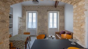 A rustic room with stone walls, a dining table with chairs, a sofa, and two windows with curtains. - Small renovated house with terrace in the heart of St Pierre d'Oléron (Saint Pierre d'Oléron)