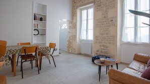 A spacious living area with a stone wall, a dining table with chairs, a sofa, and a bookshelf. - Small renovated house with terrace in the heart of St Pierre d'Oléron (Saint Pierre d'Oléron)
