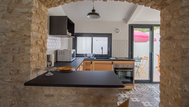 A kitchen with stone walls, a black countertop, wooden cabinets, a microwave, and a view of the outside. - Small renovated house with terrace in the heart of St Pierre d'Oléron (Saint Pierre d'Oléron)