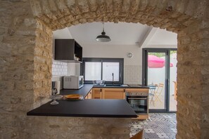 A kitchen with stone walls, a black countertop, wooden cabinets, a microwave, and a view of the outside. - Small renovated house with terrace in the heart of St Pierre d'Oléron (Saint Pierre d'Oléron)