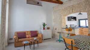 A cozy living area with a sofa, coffee table, and a dining table with chairs. A kitchen is visible through an archway, and there is a white cabinet with a plant on top. - Small renovated house with terrace in the heart of St Pierre d'Oléron (Saint Pierre d'Oléron)