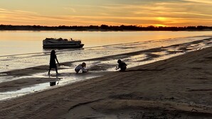Uma praia com um barco na água e pessoas brincando na areia.