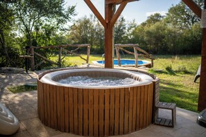 Ein Whirlpool mit Holzrahmen, ein kleiner Holztisch und ein Schwimmbecken im Hintergrund.