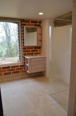 Ein Badezimmer mit Backsteinwand, Fenster, Spiegel, Waschbecken und Dusche.