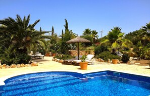 A swimming pool with lounge chairs and umbrellas, surrounded by tropical plants and a stone wall. - Finca Alqueria Fosca (Campos, Spain, Mallorca)