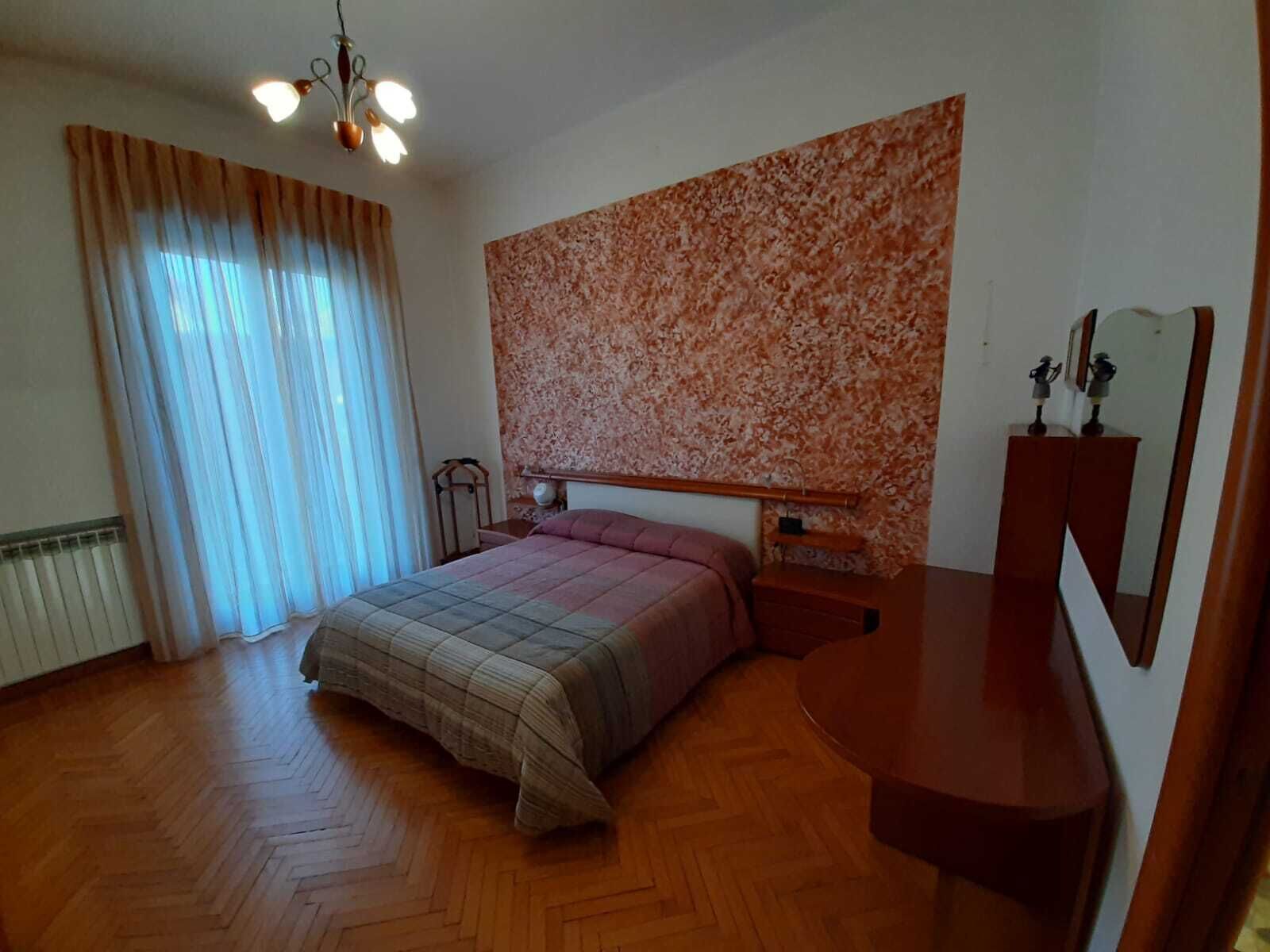 A bedroom with a bed, a nightstand, a dresser, a mirror, and a ceiling light fixture.