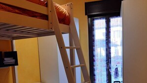A room with a bunk bed, a desk with drawers, a ladder, and a window with curtains.