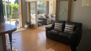 A living room with a black leather sofa, a wooden dining table, and a sliding glass door leading to a patio.