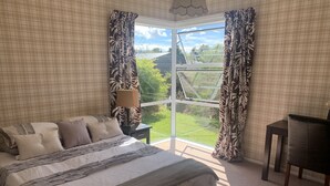 A bedroom with a large bed, a nightstand, a lamp, and a view of the outdoors through a window.