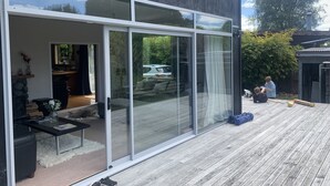 A modern house with large sliding glass doors, a wooden deck, and a stone wall.